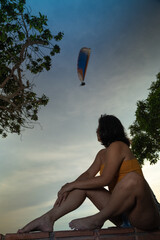 Young woman relaxing on boardwalk at sunset watching paraglider