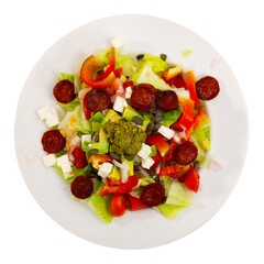 Appetizing salad of fresh vegetables with chorizo, feta avocado and pesto sauce served on platter. Isolated over white background