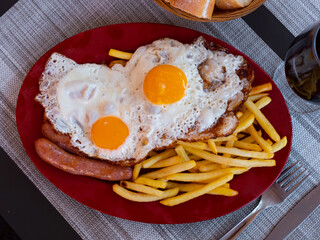 Grilled sausages, French fries and fried egg sunny side up dished up in a plate on the laid restaurant table
