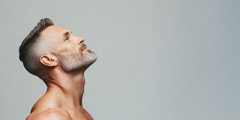 Fabulous at any age. Profile portrait of charismatic muscular 50 years old man standing over light gray background and smiling. Perfect haircut and body. Close-up. Copy-space. Studio shot
