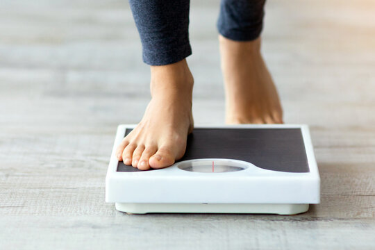 Unrecognizable young Indian woman stepping on scales to measure her weight at home, closeup of feet. Cropped view of millennial lady checking result of her slimming diet. Healthy living concept