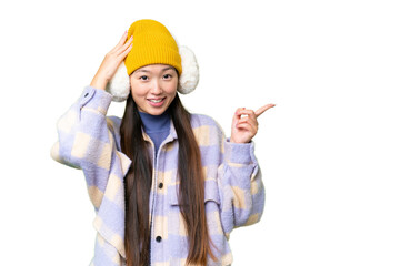 Young Asian woman wearing winter muffs over isolated chroma key background surprised and pointing finger to the side