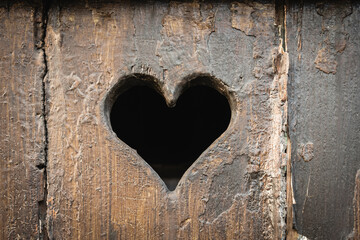 Heart-shaped hole in weathered wooden surface captures attention and evokes emotion in rustic setting
