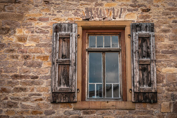 Obraz premium Rustic wooden window framed by aged stone wall reflects calm sky in a quaint rural setting