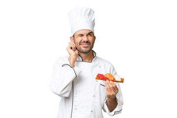 Young caucasian chef holding a sushi over isolated background frustrated and covering ears