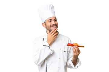 Young caucasian chef holding a sushi over isolated background looking up while smiling
