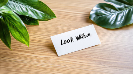 Inspirational card with "Look Within" on wood desk near green leaves