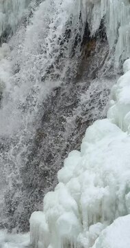 Vertical slow motion close up of a icy waterfall, river, flowing with snow and ice along each side 23.976 FPS Frames / Second, Iphone 16 Pro
