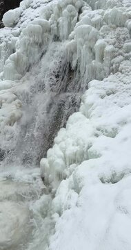 Vertical slow motion close up of a icy waterfall, river, flowing with snow and ice along each side 29.97 FPS Frames / Second, 	Iphone 16 Pro
