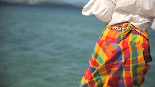 Caribbean woman dancing in front of the sea in traditional clothes (madras)