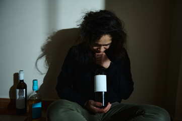 Woman sitting on floor holding wine bottle with a concerned expression