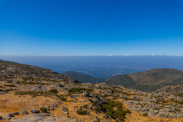 Fototapeta premium A vast mountain landscape with rocky terrain, sparse vegetation, and a distant panoramic view under a clear blue sky