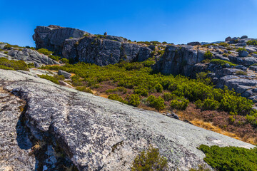A rocky mountain landscape with large granite formations and patches of green vegetation under a clear blue sky.