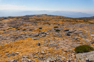 A rocky, barren mountain summit with sparse vegetation under a hazy sky, showcasing a rugged natural landscape