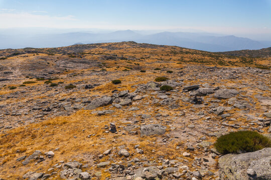 A rocky, barren mountain summit with sparse vegetation under a hazy sky, showcasing a rugged natural landscape - Powered by Adobe