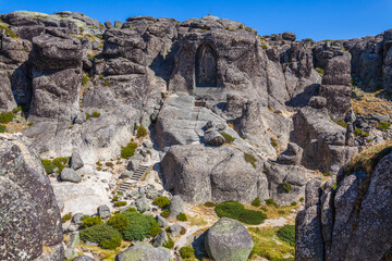 A carved image within a rock face, accessed by stone steps, creates a sense of sacred space and history against a clear blue sky