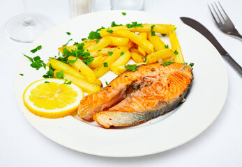 Italian dish of tasty steak of baked salmon with french fries on plate