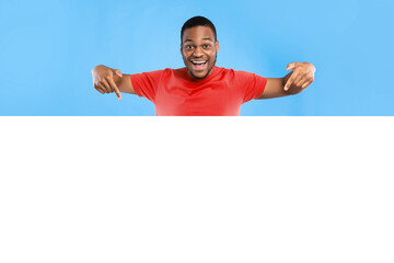 Look Here. Excited Black Man Pointing At Empty White Board For Text Advertising Great Offer Smiling To Camera Over Blue Studio Background. Sales Advertisement Mockup