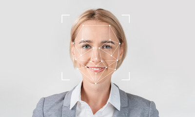 A professional woman smiles while facial recognition technology analyzes her features. She stands against a plain background, highlighting the tech's identification capabilities.