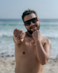 male person with beard and sunglasses doing exercises on the beach with bare torso 
