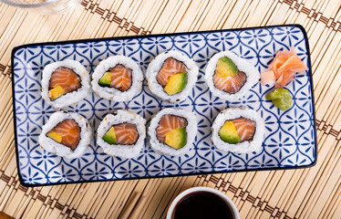 Juicy california roll on a plate with chopsticks, wasabi and soy sauce