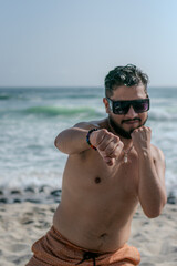 male person with beard and sunglasses doing exercises on the beach with bare torso 