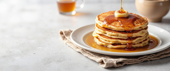 Delicious pancakes topped with butter and dripping maple syrup, evoking a warm and inviting breakfast scene, placed on a textured cloth beside a cup of syrup