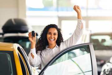 Emotional brunette woman buying new cute car, raising hand up with automatic key and smiling,...