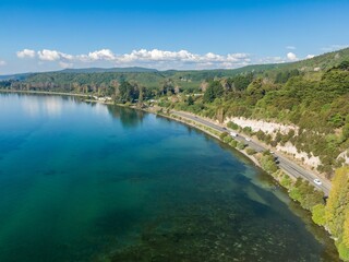 Obraz premium Aerial view of a scenic Lake Taupo road. Cars travel along the highway bordering the clear turquoise water. Tranquil landscape. LAKE TAUPO, TURANGI, WAIKATO, NEW ZEALAND