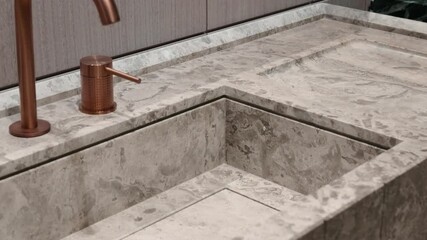 Close up of marble sink with copper faucet and soap dispenser. Sink and countertop made of same marble material giving it seamless and luxurious look.