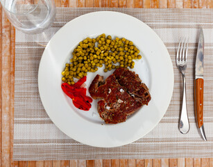 Delicious grilled beef served with peas and peppers on plate..