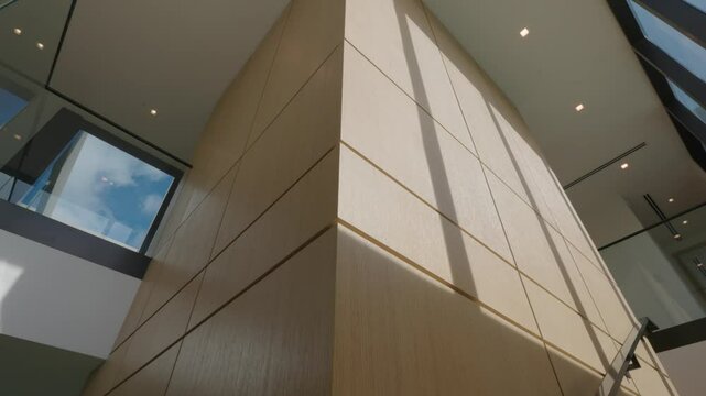 Interior of a modern building with large wooden-paneled wall as focal point. Wall composed of rectangular panels and illuminated by natural light coming through large windows