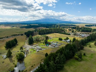 High-angle view of a rural farm, featuring buildings, pastures, and a mountain backdrop. Tranquil countryside scene. WAIOURU, MANAWATU-WANGANUI, NEW ZEALAND