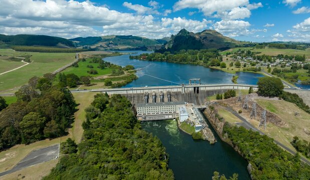 Aerial view of a hydroelectric dam, showcasing the power station and reservoir. Green hills and valleys surround the Waikato River. WHAKAMARU DAM, WHAKAMARU, WAIKATO, NEW ZEALAND