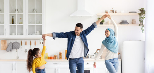 Cheerful arab family of three dancing in kitchen together, having fun at home. Happy middle eastern...