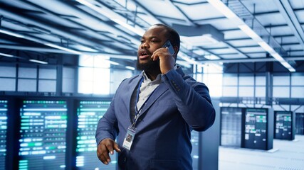 Fototapeta premium IT support worker in data center talking in phone call, doing yearly checkup. On field engineer chatting with manager in server hub during telephone call, monitoring servers infrastructure, camera B