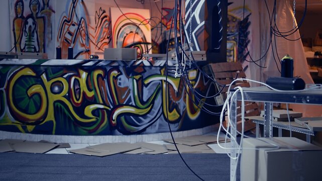 Desolate headquarters used by gang members with graffiti drawings sprayed on walls. Rubble in ghetto hideout after criminals rushed to evacuate place, dolly in camera shot