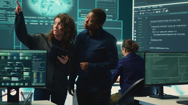 Cyber security experts women working on spyware and malware detection in a governmental agency. Examining server information on a big screen to combat cyberterrorism and cyberwarfare. Camera A.