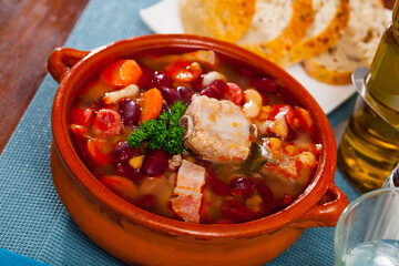 Appetizing beans stewed with pork, carrots and corn garnishing with fresh green in clayware