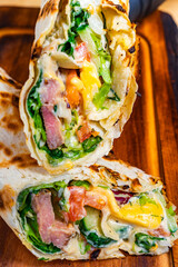 Freshly made wrap filled with vegetables and proteins on wooden board