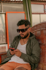 male person seated in his rocking chair with glasses working from his cell phone on his terrace 