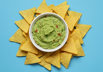 Fresh guacamole sauce in bowl with Mexican corn chips over bright blue background, top view with free space fot text