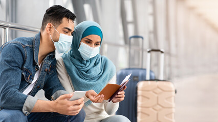 Muslim Couple In Medical Masks Waiting For Flight In Airport Terminal, Islamic Spouses Checking...