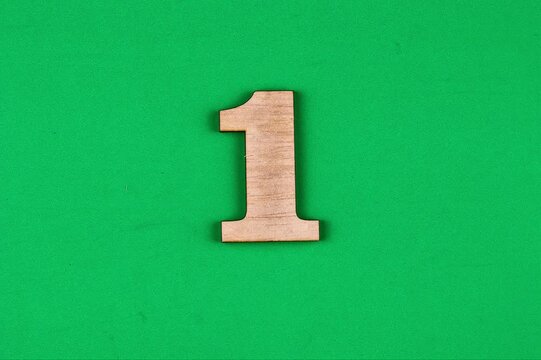 A close-up of a light brown wooden numeral "1" positioned against a vibrant green textured surface.
