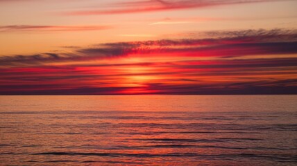Fototapeta premium A breathtaking sunset over calm waters, showcasing vibrant hues of red, orange, and purple, creating a serene and peaceful atmosphere.