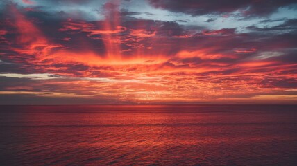 A stunning sunset over the tranquil ocean, showcasing vibrant reds and oranges splashed across the sky, creating a breathtaking natural spectacle.