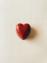Fototapeta premium Red Heart-Shaped Chocolate: A simple yet striking photo of a single, perfectly shaped red heart-shaped chocolate captured from a top-down angle on a smooth white background