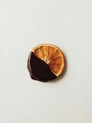 Naklejka premium Dried Orange Chocolate Coated: A simple yet striking photo of a single slice of dried orange delicately dipped in glossy dark chocolate, placed against a pure white background