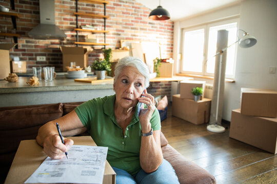 Senior woman on phone reviewing paperwork at home with moving boxes