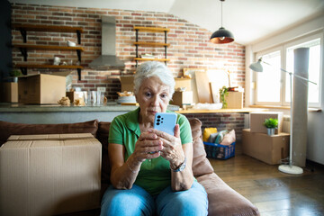 Senior woman on phone reviewing paperwork at home with moving boxes